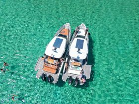 A vibrant scene featuring two boats anchored in crystal-clear turquoise waters, with guests enjoying the sun and swimming nearby — perfect for a fun day on the water.