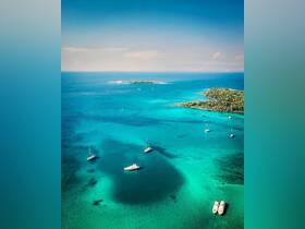 A stunning aerial view of several yachts anchored in crystal-clear turquoise waters, showcasing the beauty of a tropical paradise.