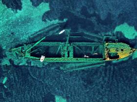 An aerial view of a shipwreck surrounded by clear waters, with snorkelers exploring the site — a captivating underwater adventure for diving enthusiasts.