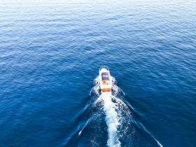 An aerial view of a speedboat cruising through calm blue waters, showcasing the sleek design and vibrant colors of the vessel.