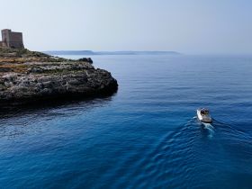 A scenic aerial view of a boat cruising through calm waters near a rocky coastline, showcasing the beauty of maritime exploration.