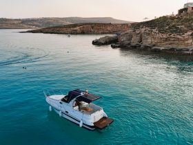 A stunning aerial view of a boat cruising through crystal-clear waters, surrounded by picturesque cliffs — perfect for exploring coastal destinations.