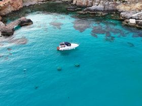 Aerial view of a sleek boat cruising through crystal-clear turquoise waters, surrounded by rocky cliffs — a perfect scene for exploring coastal beauty.