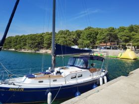 A beautiful sailboat docked at a serene waterfront, surrounded by lush greenery, perfect for a relaxing day on the water.