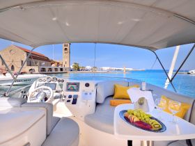 A beautifully arranged interior of a boat featuring a helm and seating area, complemented by a platter of fresh fruit and drinks — perfect for a luxurious day on the water.