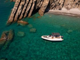 A stunning aerial view of a speedboat cruising through crystal-clear waters, framed by dramatic rocky cliffs — perfect for exploring coastal destinations.