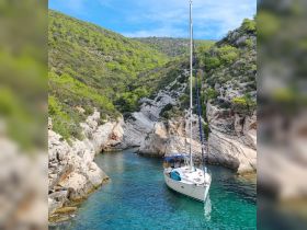 A serene view of a sailboat anchored in a picturesque cove, surrounded by lush greenery and clear turquoise waters, perfect for exploring hidden gems along the coastline.