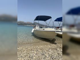 A scenic view of a boat docked on a sandy beach, surrounded by clear turquoise waters and mountains in the background, perfect for a relaxing day on the water.