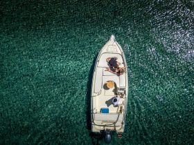 An aerial view of a couple enjoying their time on a boat in crystal-clear waters, perfect for a relaxing day on the water.
