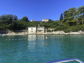A picturesque view of a serene coastline with a beach house, showcasing clear turquoise waters and a swimmer enjoying the sun — perfect for a relaxing day by the sea.