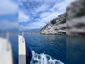 A scenic view of a boat cruising through clear blue waters, showcasing the stunning rocky coastline and vibrant sky — perfect for exploring coastal destinations.