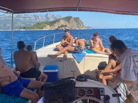 A lively group enjoys a sunny day on a boat, relaxing and sunbathing while taking in the beautiful coastline views — perfect for summer adventures on the water.