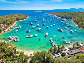 A stunning aerial view of a vibrant harbor filled with boats, surrounded by lush greenery and crystal-clear turquoise waters — a perfect destination for boating enthusiasts and beach lovers.