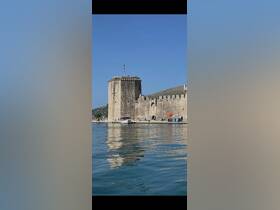 A view of a historic castle by the water, with reflections visible in the calm sea. The image lacks clarity and detail.