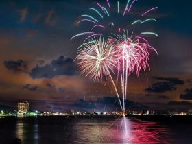 A stunning display of fireworks lights up the night sky over the city, creating a vibrant backdrop for celebrations on the water.