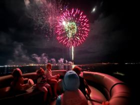 A group of children and adults enjoy a spectacular fireworks display from the comfort of their boat, creating a memorable night of celebration on the water.