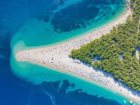A stunning aerial view of a vibrant beach filled with sunbathers and turquoise waters, showcasing the beauty of coastal destinations perfect for summer getaways.