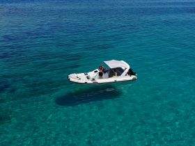 A group enjoys a sunny day on a boat anchored in crystal-clear turquoise waters, perfect for swimming and relaxation.