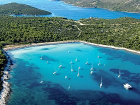 A stunning aerial view of a tranquil bay dotted with sailboats, surrounded by lush greenery and crystal-clear waters, perfect for sailing adventures and island exploration.
