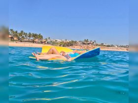 Two friends relax on a floating mat in crystal-clear waters, enjoying a sunny day at the beach — a perfect scene for summer fun and relaxation.