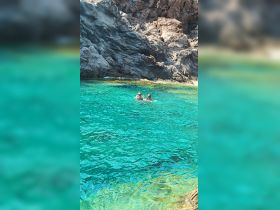 A couple enjoys a refreshing swim in crystal-clear waters against a stunning rocky backdrop, perfect for adventure seekers and nature lovers.