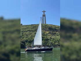A sailing group enjoys a scenic trip with the iconic Christ the King statue in the background, showcasing the beauty of the landscape and maritime adventure.