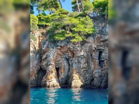 A stunning view of rocky cliffs adorned with lush greenery, set against the backdrop of crystal-clear turquoise waters — a perfect representation of coastal beauty.