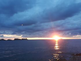 A stunning sunset casts a golden glow over the coastline, creating a picturesque view perfect for romantic evenings or serene boat trips.
