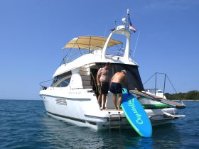 Two men prepare for paddleboarding off the back of a luxury yacht, showcasing a fun day on the water.