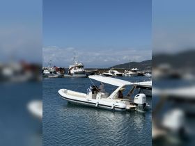 A sleek speedboat is docked in a marina, showcasing its design against a backdrop of other vessels and a clear blue sky.