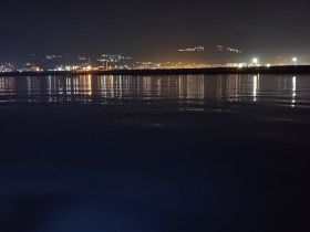 A nighttime view of a waterfront with city lights reflecting on the water, creating a serene atmosphere.