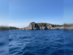 A stunning view of a rocky coastline under a clear blue sky, showcasing the natural beauty of the area — perfect for island hopping adventures.