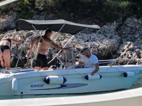 A group of individuals interacts on a boat near rocky shores, showcasing a lively day on the water.