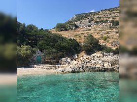 A picturesque view of a serene beach with crystal-clear waters and a rocky coastline, showcasing the natural beauty of the area — perfect for a relaxing getaway.