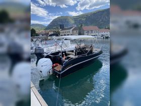 A sleek boat docked in a picturesque marina, surrounded by lush mountains and clear waters, perfect for exploring coastal destinations.