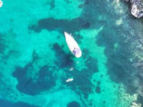 An aerial view captures a boat anchored in stunning turquoise waters, with people enjoying the water nearby — a perfect scene for a summer adventure.