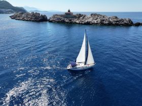 A stunning aerial view of a sailboat gracefully navigating through crystal-clear waters, with rocky shores and a lighthouse in the background, perfect for showcasing sailing adventures.
