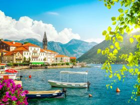 A picturesque view of a charming harbor surrounded by mountains, showcasing colorful boats and vibrant flowers — a perfect destination for scenic boat tours.
