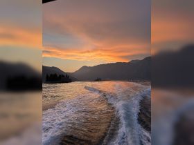 A stunning sunset view over the mountains and islands, with the boat's wake creating a beautiful reflection on the water — a perfect moment for nature lovers and photographers.
