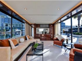 A luxurious interior view of a boat's lounge area, featuring elegant seating and large windows overlooking the marina, perfect for relaxing and enjoying the waterfront ambiance.