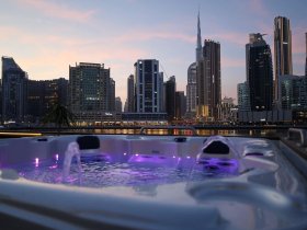 A luxurious jacuzzi with purple lighting overlooks the stunning Dubai skyline at dusk, perfect for relaxing after a day on the water.