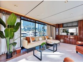 A beautifully designed interior of a boat featuring a cozy lounge area with modern furnishings and large windows offering views of the marina.