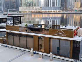 A stunning view of the 'Into The Blue' houseboat docked, showcasing its modern design and luxurious amenities against a city backdrop.