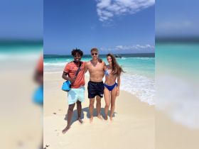 A joyful group poses on the beach, enjoying a sunny day by the turquoise waters — perfect for memorable summer adventures.