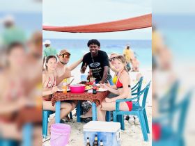 A lively group enjoys a beach meal together, showcasing a fun and festive atmosphere perfect for family gatherings or beach parties.