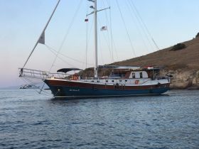 A beautiful yacht, 'La Perla C', docked in calm waters, showcasing its elegant design against a serene backdrop.