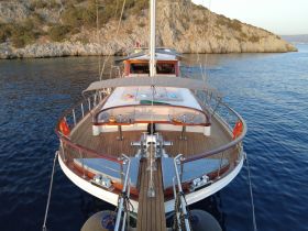 A stunning view of a yacht from the front, showcasing its elegant design against a serene backdrop of rocky cliffs and calm waters.