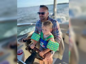 A father and his young son enjoy a boating experience together, with the child actively participating at the helm, creating cherished family memories on the water.