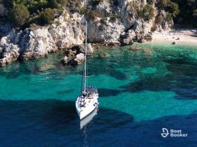 An aerial view of a sailboat anchored near a stunning beach, with swimmers enjoying the crystal-clear waters — a perfect scene for a summer getaway.