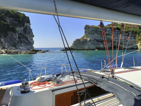 A serene view from the interior of a sailboat, showcasing the helm and the stunning coastal scenery outside — perfect for a relaxing day on the water.